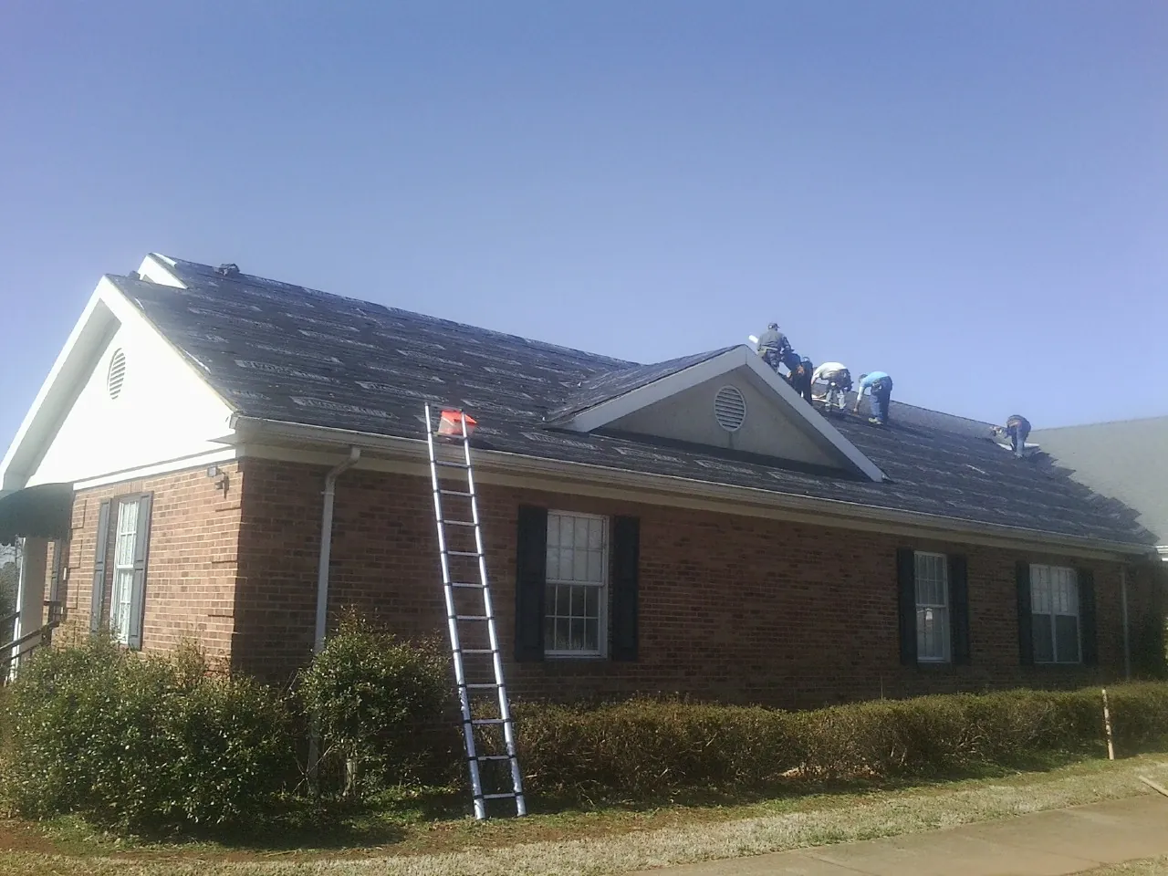 Crew tearing shingles off a brick ranch roof with a ladder set — Emergency Roof Repair work by our crew in Wausaukee