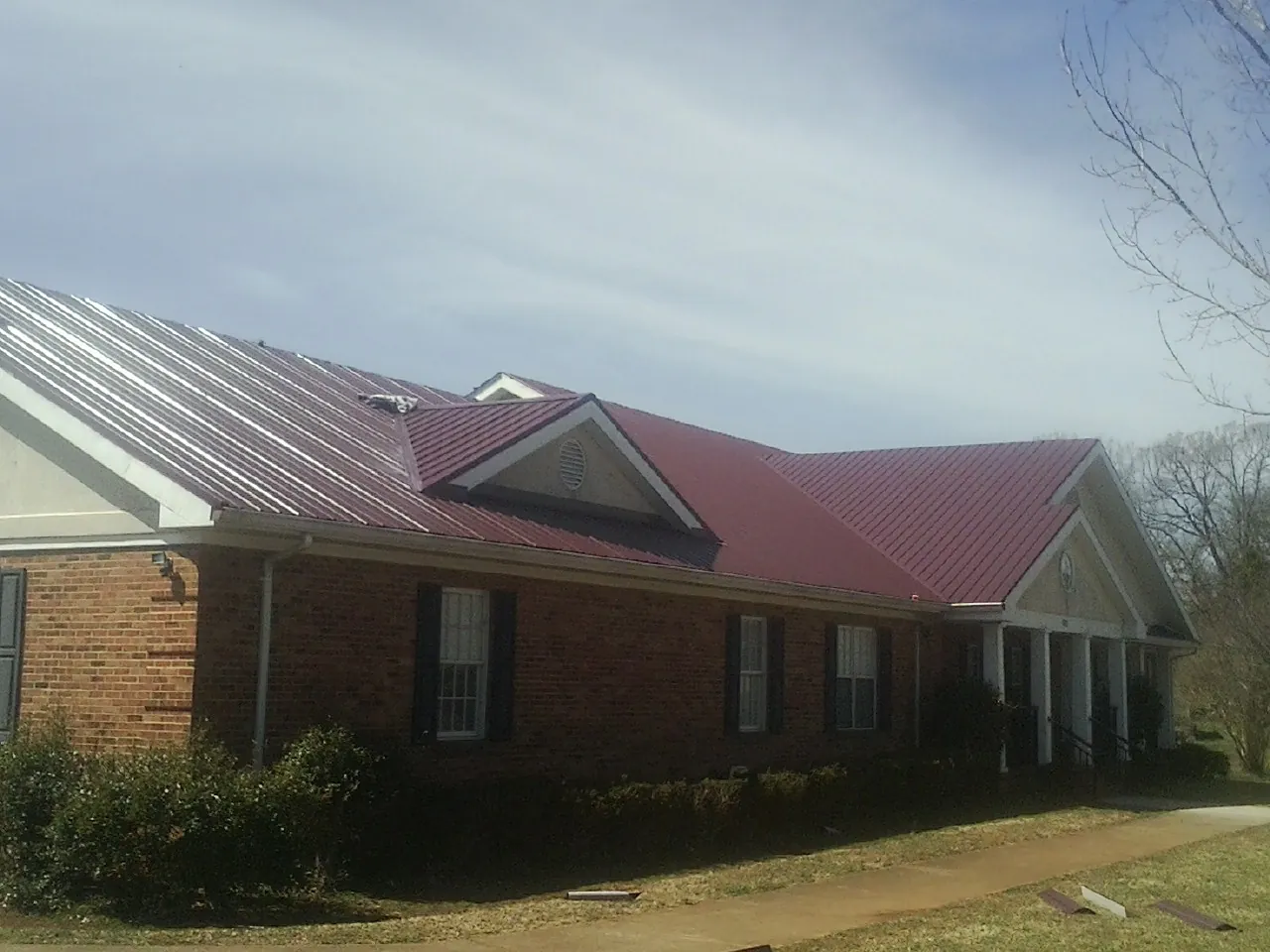 Red metal roof with gabled entries on a long brick building, from a Hail Damage Roof Repair job in Wausaukee