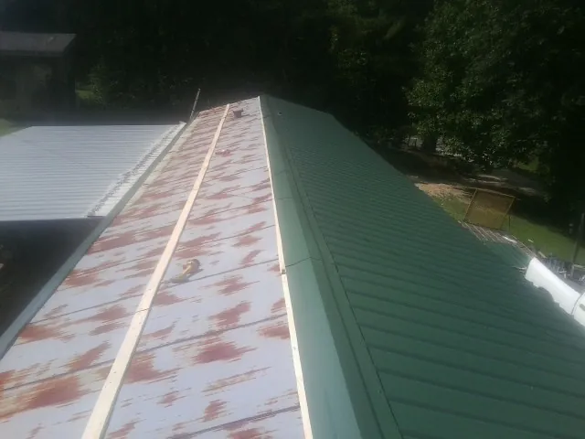 Old rusted panels beside newly installed green metal roofing — Wind Damage Roof Repair by Roofing Brothers in Wausaukee