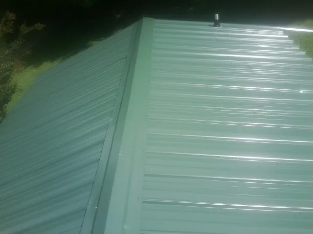 New green metal panels meeting at the ridge of a roof — Flat Roof Repair work by our crew in Wausaukee