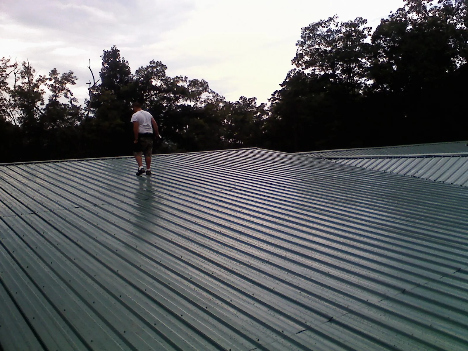 Roofer walking a wide expanse of new green metal roofing in Wausaukee