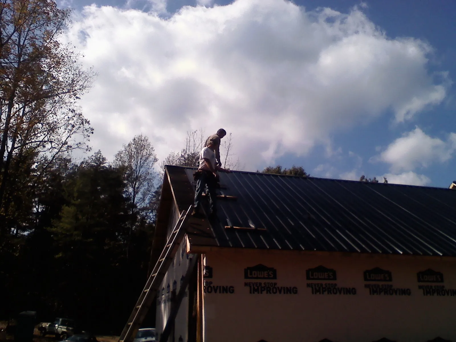Roofer fastening dark metal panels high against a cloudy sky, from a Roof Inspection job in Wausaukee