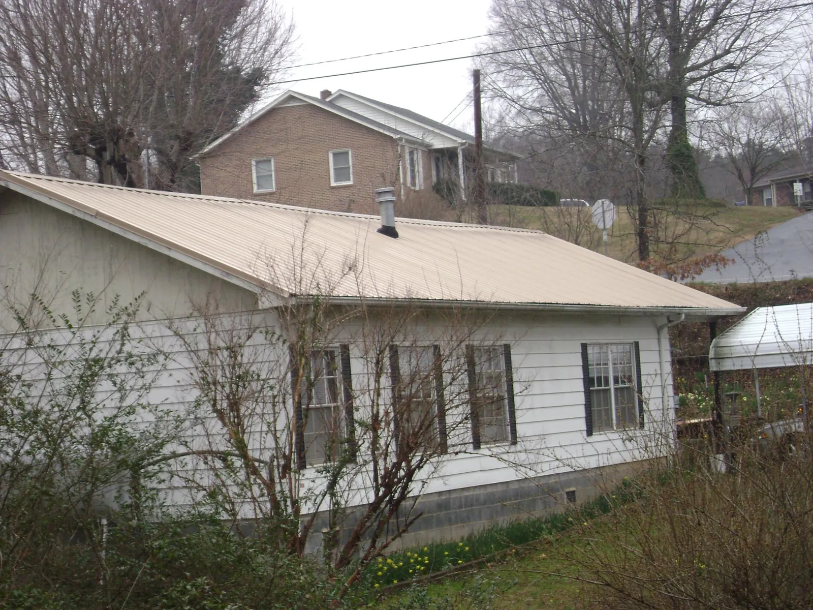 Tan metal roof on a white sided house set into a hillside — Commercial Roofing by Roofing Brothers in Wausaukee