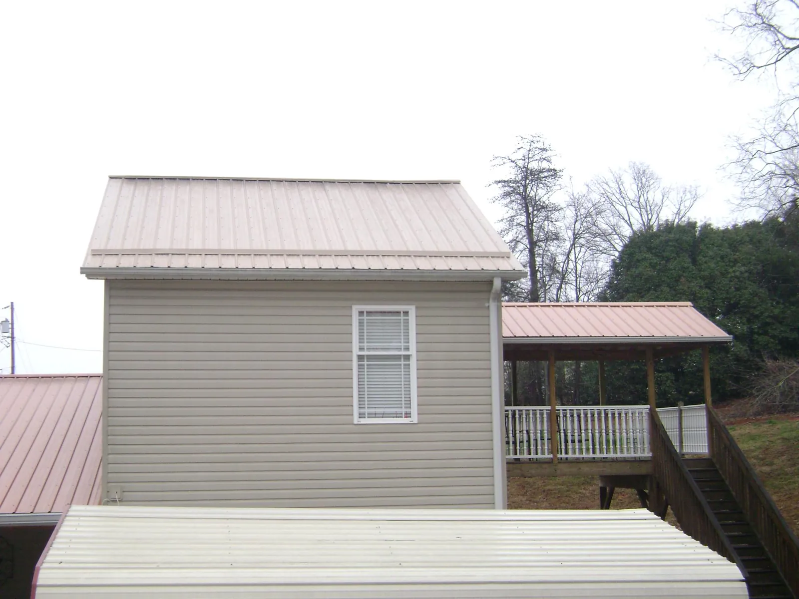 Tan metal roofs on a two story addition and attached porch, from a Roof Replacement job in Wausaukee
